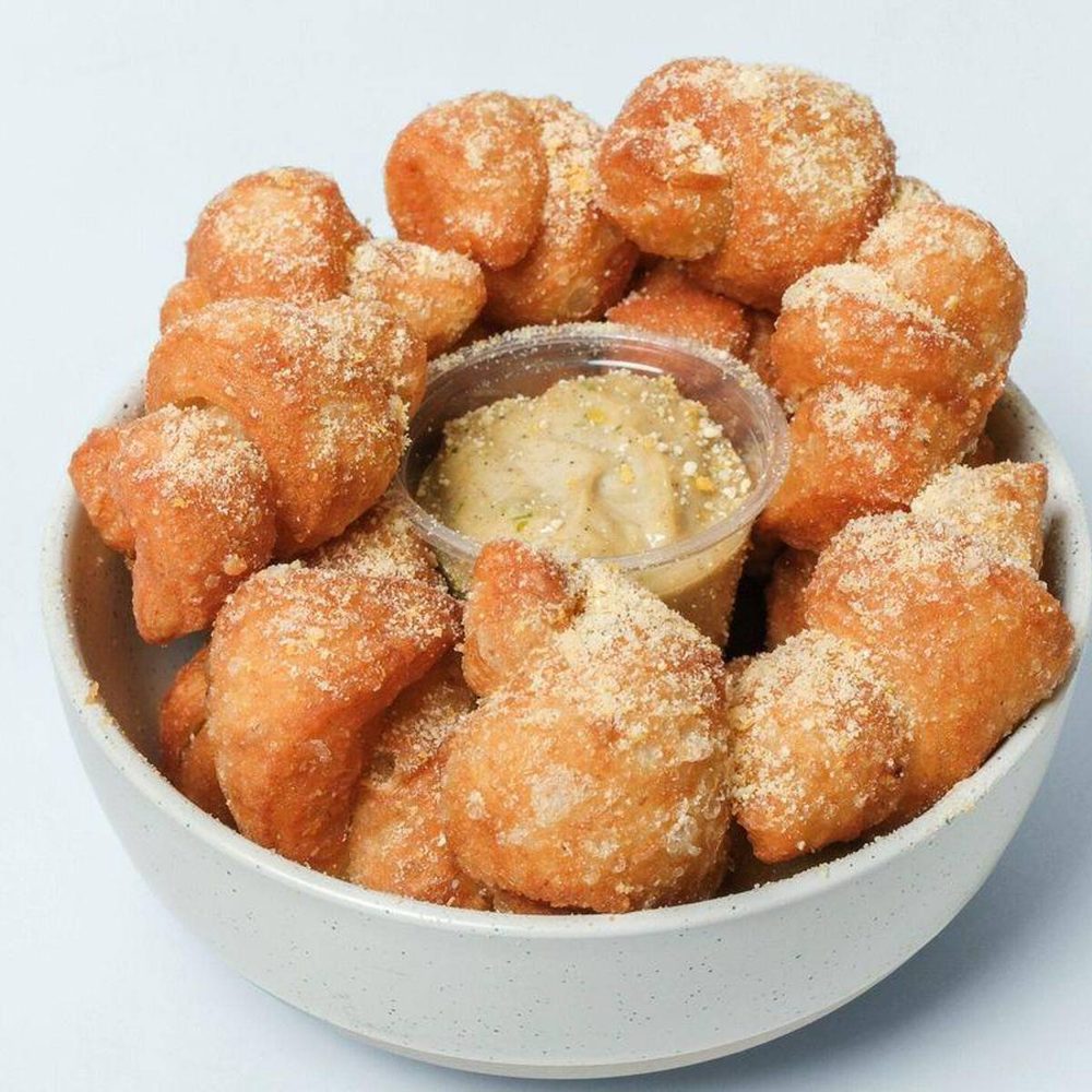 Bowl of golden garlic knots dusted with parmesan and served with dipping sauce